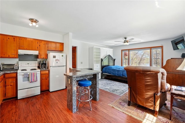 kitchen with brown cabinetry, under cabinet range hood, white appliances, and open floor plan