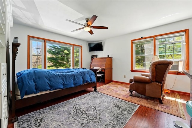bedroom featuring a ceiling fan, baseboards, wood finished floors, and cooling unit