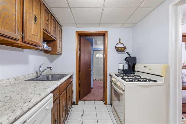 kitchen featuring white appliances, a drop ceiling, brown cabinets, a sink, and light tile patterned floors