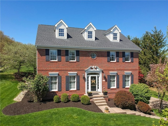 view of front of house featuring roof with shingles, brick siding, and a front yard