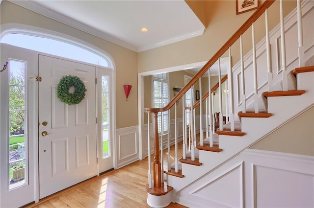 entrance foyer featuring ornamental molding, wainscoting, a decorative wall, stairway, and light wood finished floors