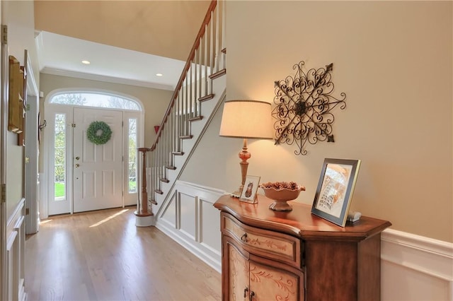 foyer featuring stairs, ornamental molding, light wood-style flooring, and a decorative wall
