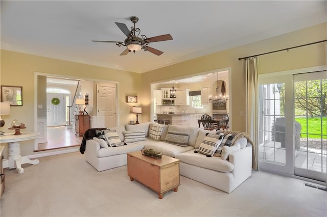 living area featuring a healthy amount of sunlight, carpet floors, ceiling fan with notable chandelier, and visible vents