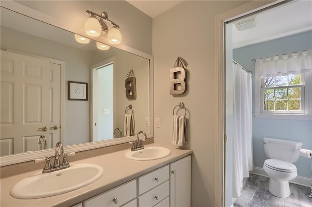 bathroom featuring double vanity, toilet, a sink, and wood finished floors