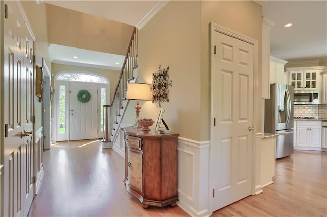 foyer entrance featuring crown molding, a decorative wall, a wainscoted wall, light wood-type flooring, and stairway