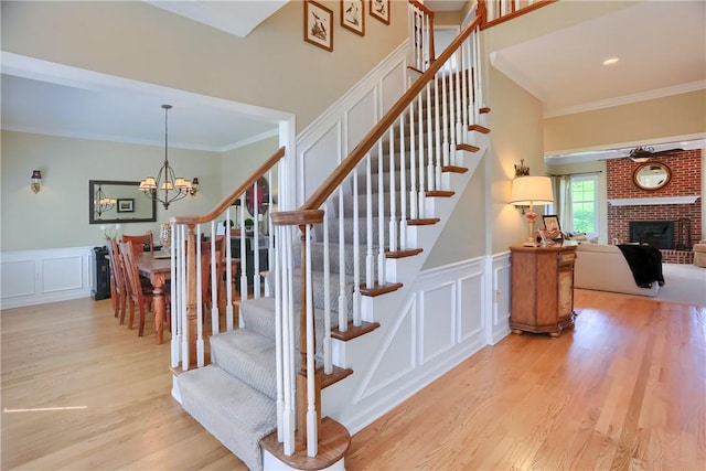 stairway with crown molding, an inviting chandelier, a decorative wall, and wood finished floors