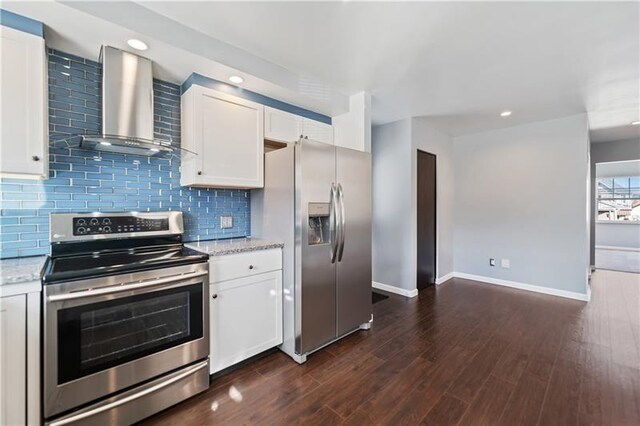 kitchen featuring baseboards, wall chimney exhaust hood, white cabinetry, tasteful backsplash, and stainless steel appliances