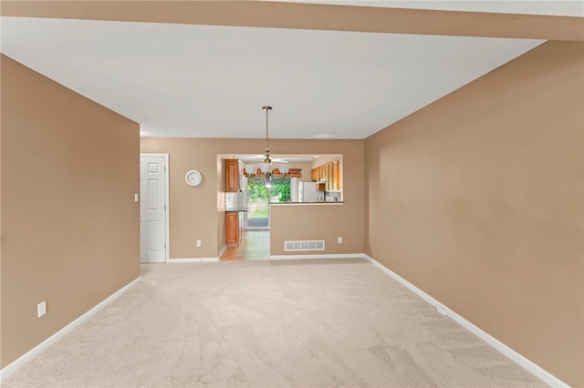 spare room featuring a chandelier, baseboards, visible vents, and light carpet