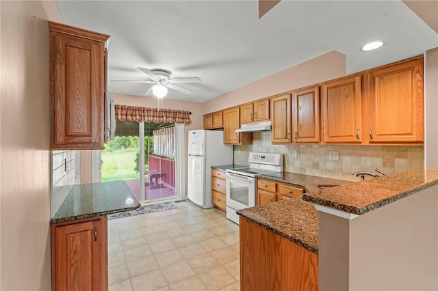 kitchen with dark stone counters, under cabinet range hood, and white appliances