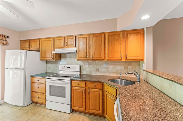 kitchen featuring brown cabinetry, backsplash, a sink, under cabinet range hood, and white appliances