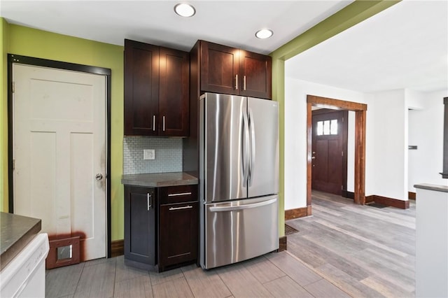 kitchen featuring white dishwasher, dark brown cabinets, freestanding refrigerator, baseboards, and tasteful backsplash