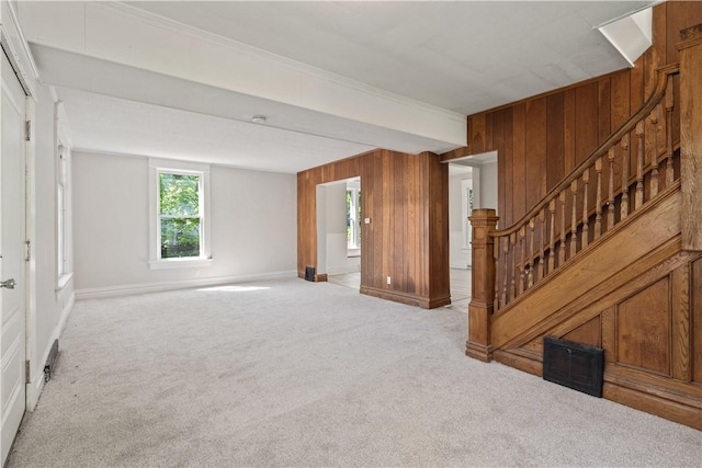 unfurnished living room featuring visible vents, carpet floors, baseboards, wooden walls, and stairway