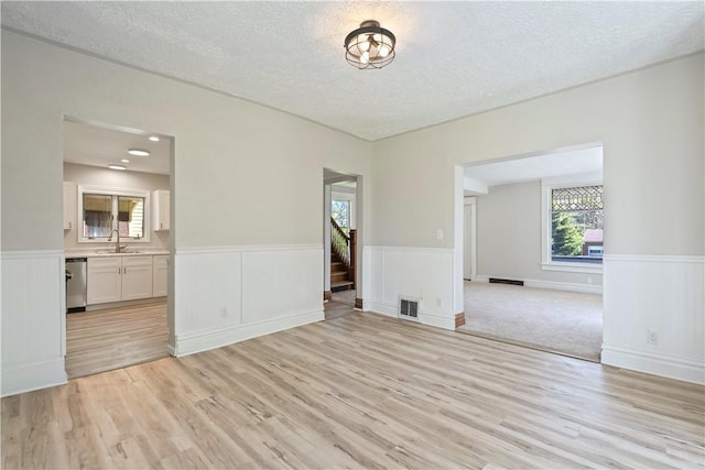 unfurnished room with visible vents, a sink, light wood finished floors, and a wainscoted wall