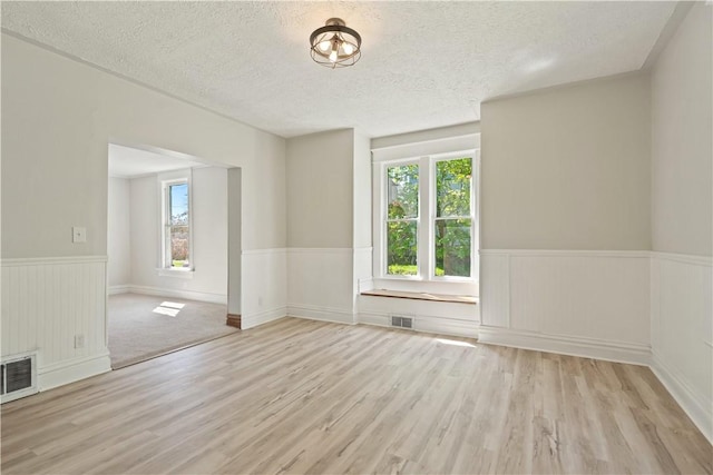 empty room with a wealth of natural light, wainscoting, and visible vents