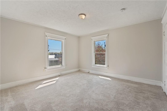 empty room featuring carpet flooring, a textured ceiling, ornamental molding, and baseboards