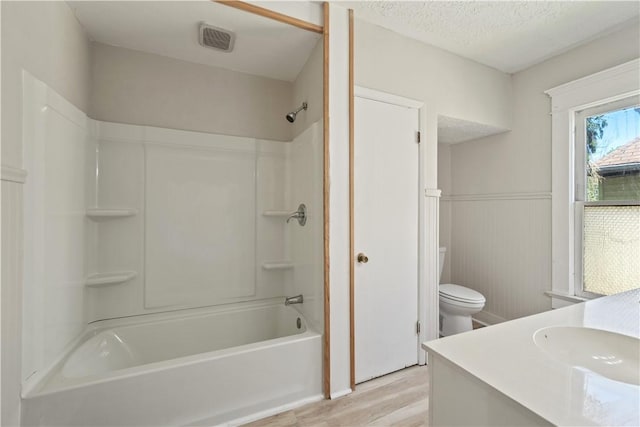 full bathroom featuring a textured ceiling, wainscoting, wood finished floors, vanity, and toilet