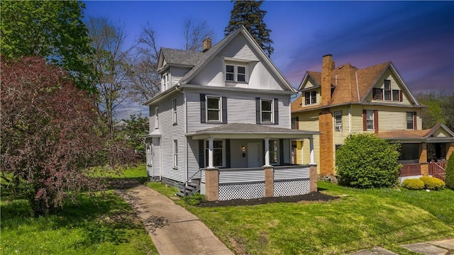 view of front of house with covered porch, a shingled roof, and a front yard