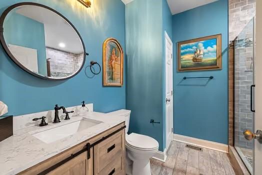 bathroom with a tile shower, wood finished floors, vanity, baseboards, and toilet