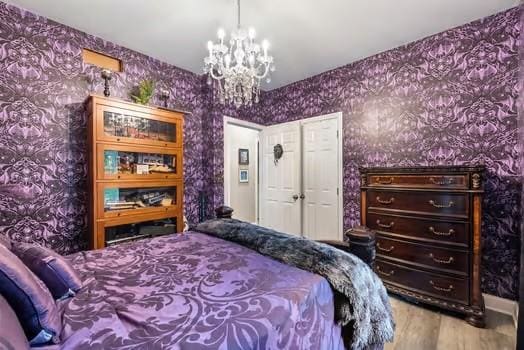 bedroom with wood finished floors, a notable chandelier, and wallpapered walls
