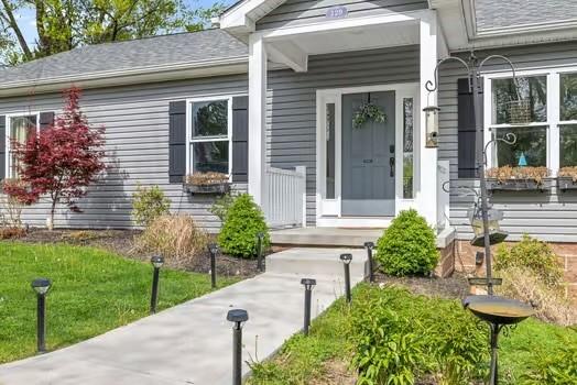entrance to property featuring roof with shingles and a yard