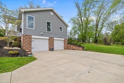 view of side of property with concrete driveway, brick siding, a lawn, and a garage