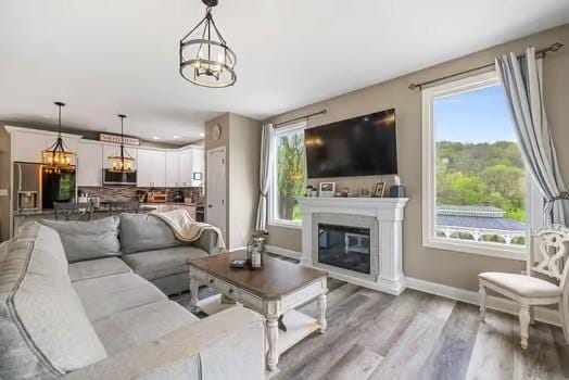 living area featuring baseboards, a glass covered fireplace, wood finished floors, and a chandelier
