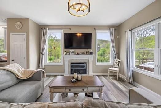 living area featuring baseboards, an inviting chandelier, a glass covered fireplace, and wood finished floors
