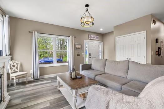 living area featuring visible vents, a fireplace, wood finished floors, baseboards, and a notable chandelier