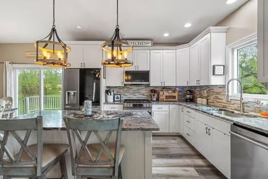 kitchen with light stone countertops, white cabinetry, a sink, backsplash, and stainless steel appliances
