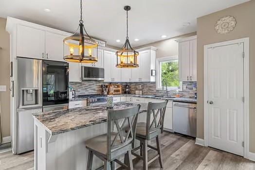 kitchen featuring appliances with stainless steel finishes, tasteful backsplash, a sink, white cabinets, and light wood finished floors
