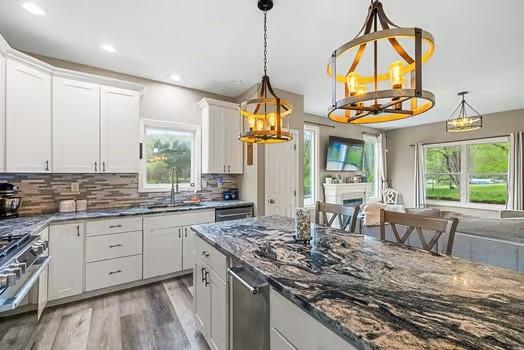 kitchen with light wood-type flooring, dark stone counters, white cabinets, a sink, and gas stove