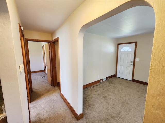 foyer entrance featuring carpet floors, arched walkways, baseboards, and visible vents