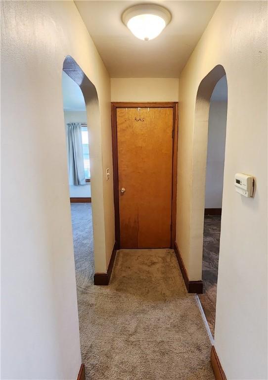 hallway with baseboards, arched walkways, and carpet flooring