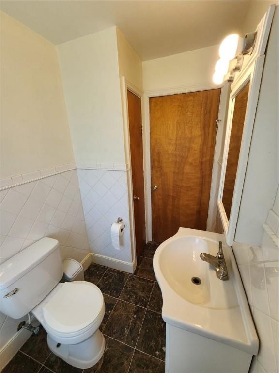 half bathroom with a wainscoted wall, tile patterned flooring, vanity, and toilet