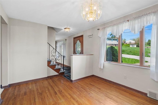 empty room with visible vents, stairway, baseboards, a notable chandelier, and light wood-style flooring