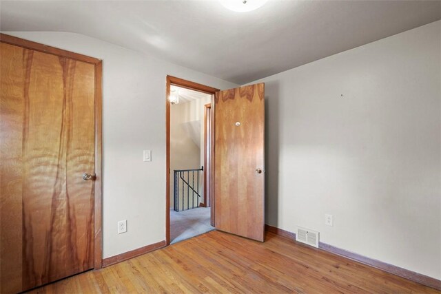 unfurnished bedroom with baseboards, visible vents, lofted ceiling, and light wood finished floors