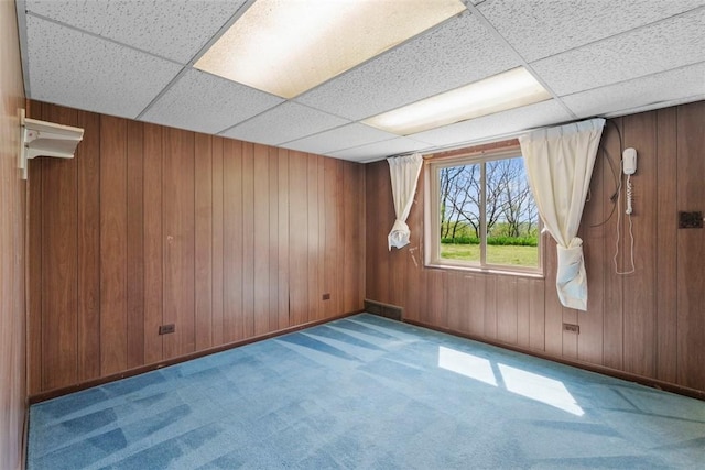 carpeted spare room featuring wooden walls and a paneled ceiling