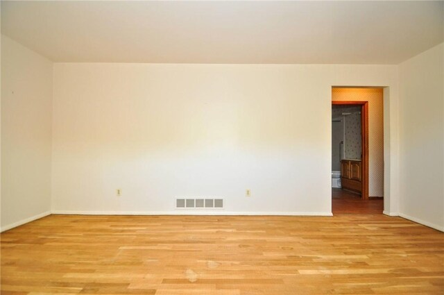empty room with visible vents, light wood finished floors, and baseboards