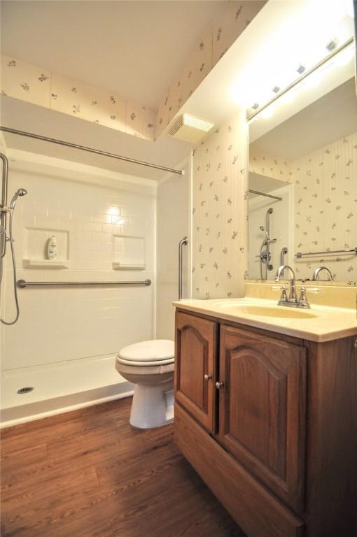 full bath with walk in shower, wallpapered walls, and wood finished floors