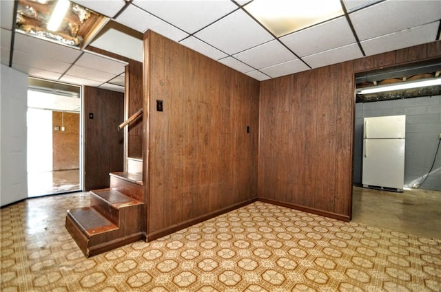 unfurnished room featuring a drop ceiling, wooden walls, and stairway
