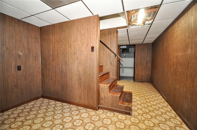 finished below grade area with wood walls, a paneled ceiling, and stairway