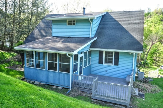 back of house featuring a yard, a deck, a shingled roof, and a sunroom