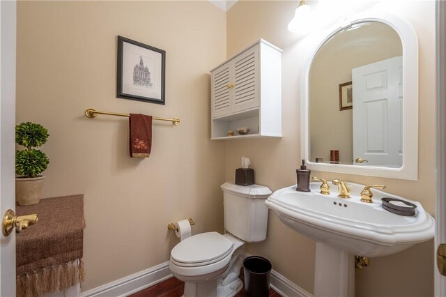 bathroom featuring baseboards, wood finished floors, and toilet