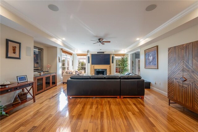 living room with ceiling fan, light wood finished floors, a fireplace, baseboards, and ornamental molding