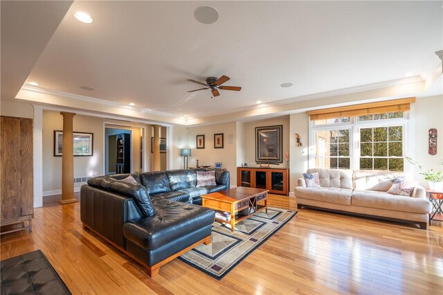 living room featuring crown molding, decorative columns, a raised ceiling, and light wood-type flooring