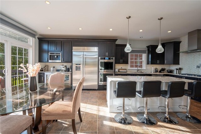 kitchen with decorative backsplash, a kitchen island, wall chimney range hood, a sink, and appliances with stainless steel finishes