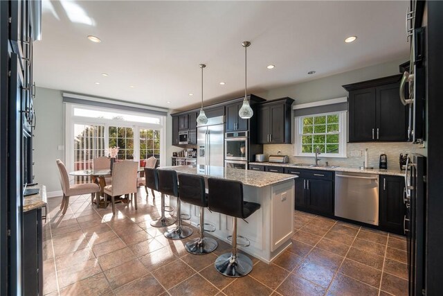 kitchen with light stone countertops, appliances with stainless steel finishes, a sink, and tasteful backsplash