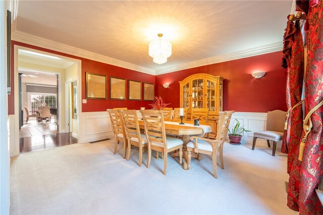 carpeted dining area with an inviting chandelier, ornamental molding, and a wainscoted wall