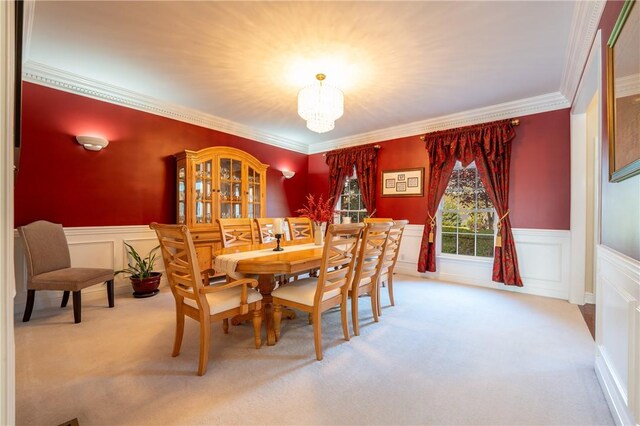 carpeted dining room with crown molding, a chandelier, and wainscoting