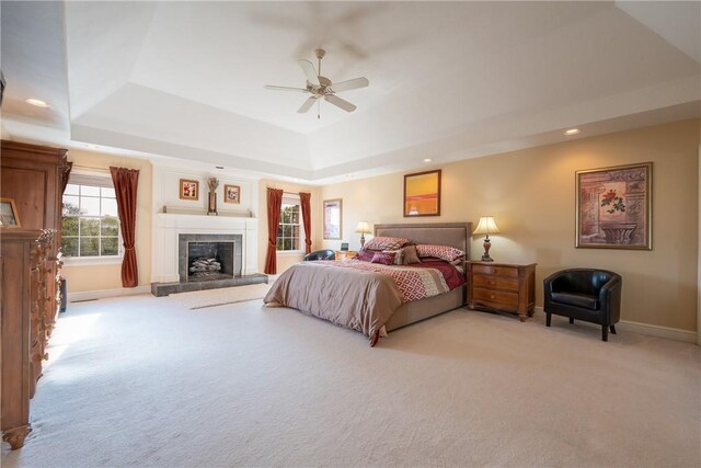 bedroom with light colored carpet, baseboards, a tray ceiling, and a fireplace